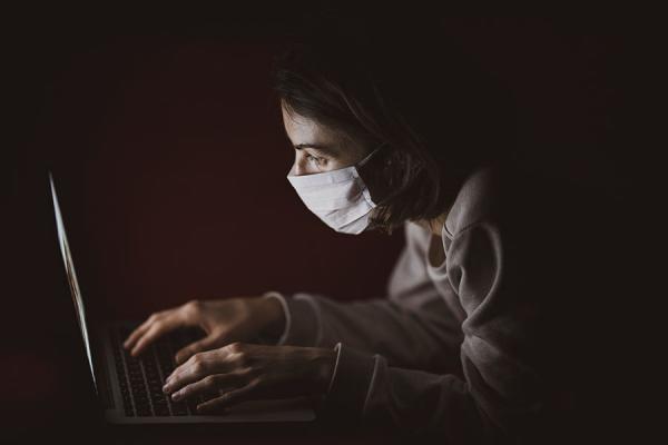 A photo of a woman wearing a surgical mask working on a laptop computer
