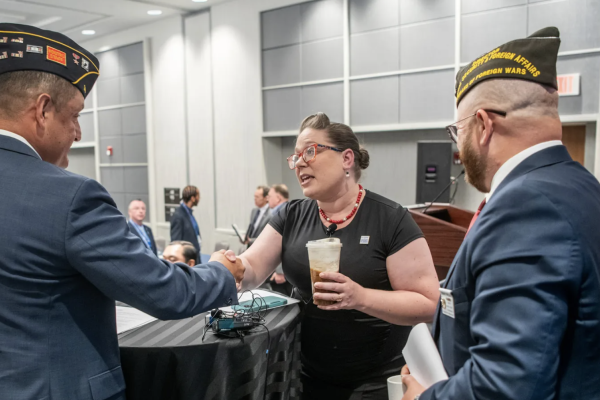 Photo of Gretchen Klingler, who is a white woman with red glasses in a black dress, shaking hands with a military official.