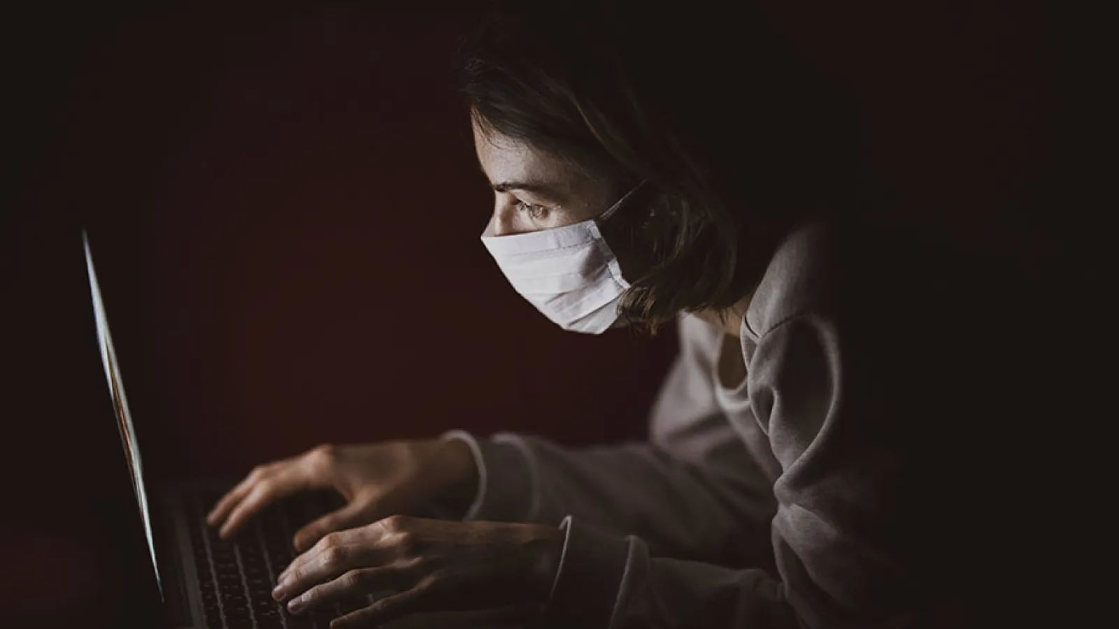 A woman wearing a surgical mask working on a laptop computer