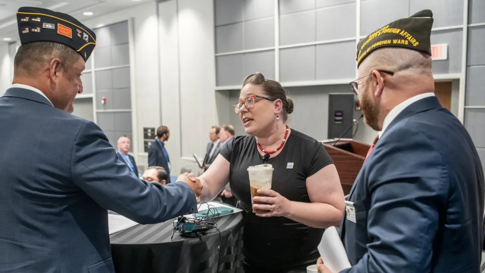 woman with red glasses in a black dress, shaking hands with a military official.