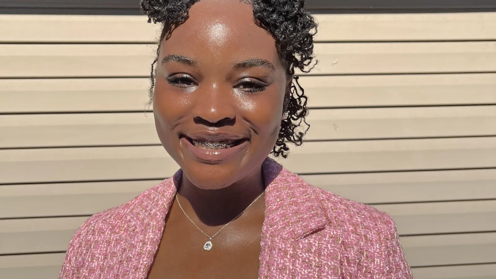 Woman with short black hair wearing a pink blazer and white shirt with a pendant necklace on.