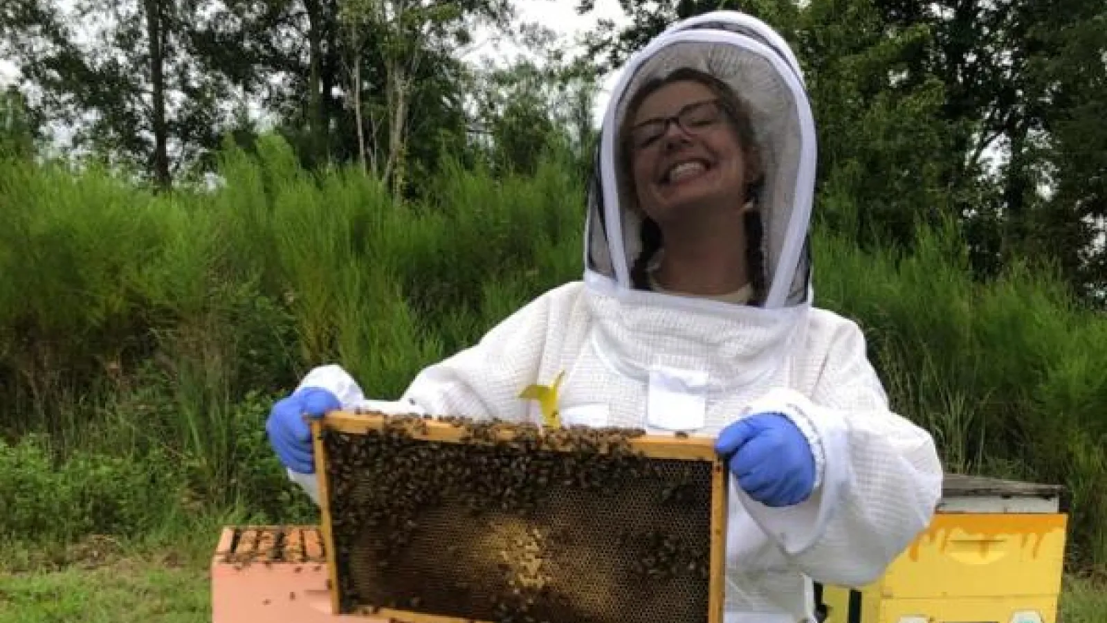 Woman in white bee keeper outfit holding a part of a beehive