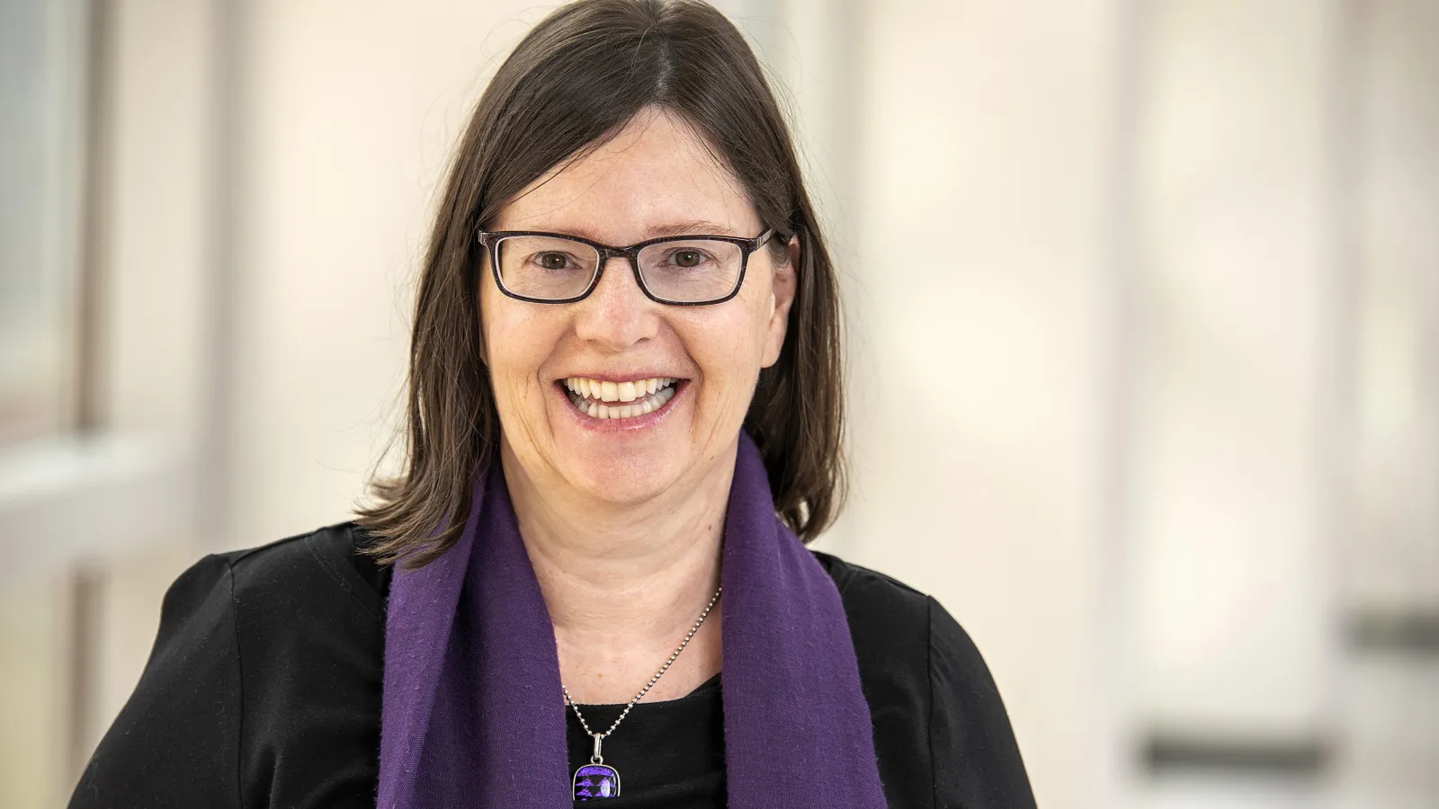 Headshot of Janet Childerhose. She is a white woman wearing glasses with shoulder length hair. She is wearing a black blouse and purple scarf
