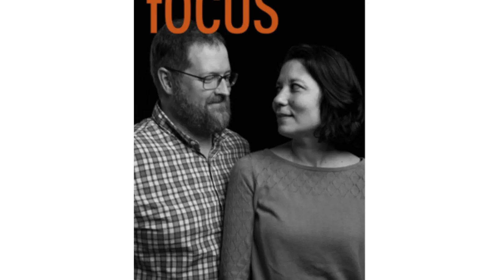 A bearded man in glasses smiling at a dark haired woman smiling up at him
