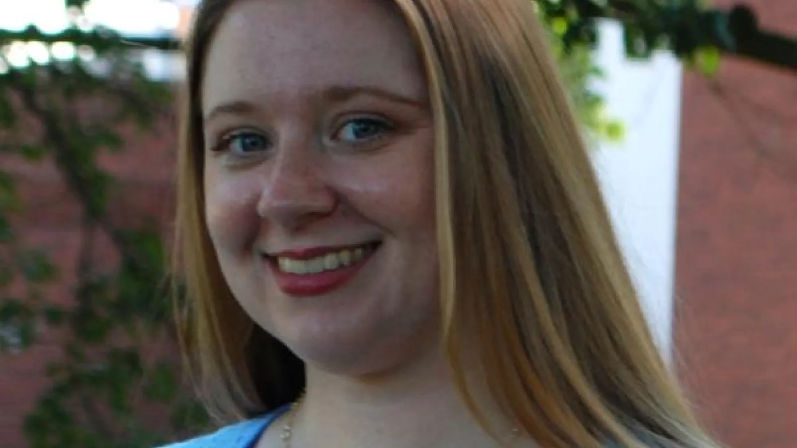 Young white woman with blonde hair and blue shirt smiling