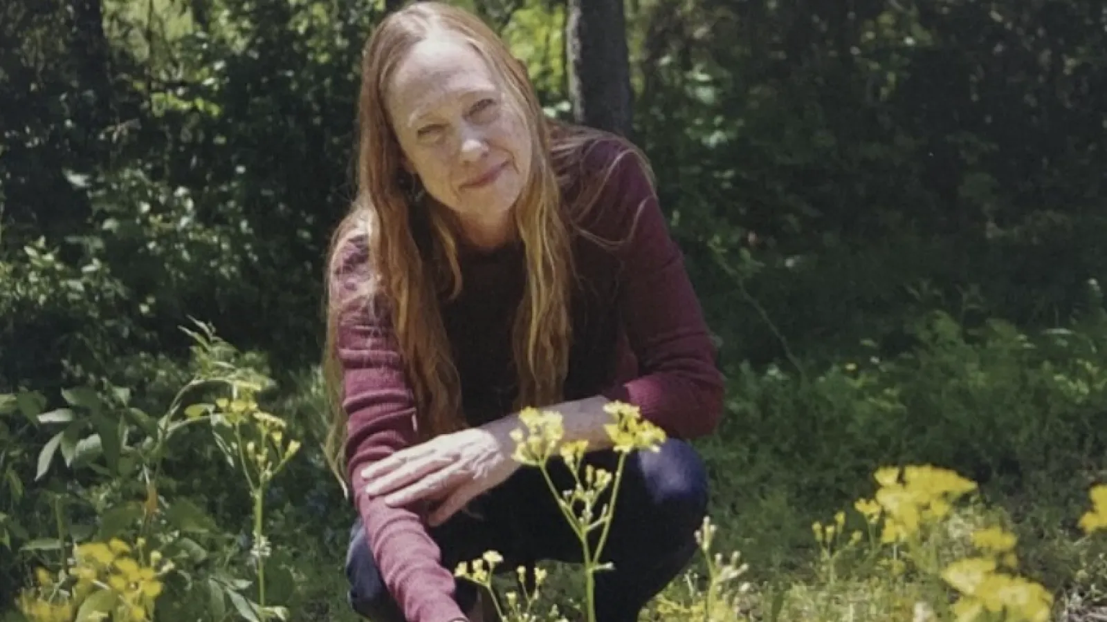 Middle aged white woman crouching down in a field of long grass
