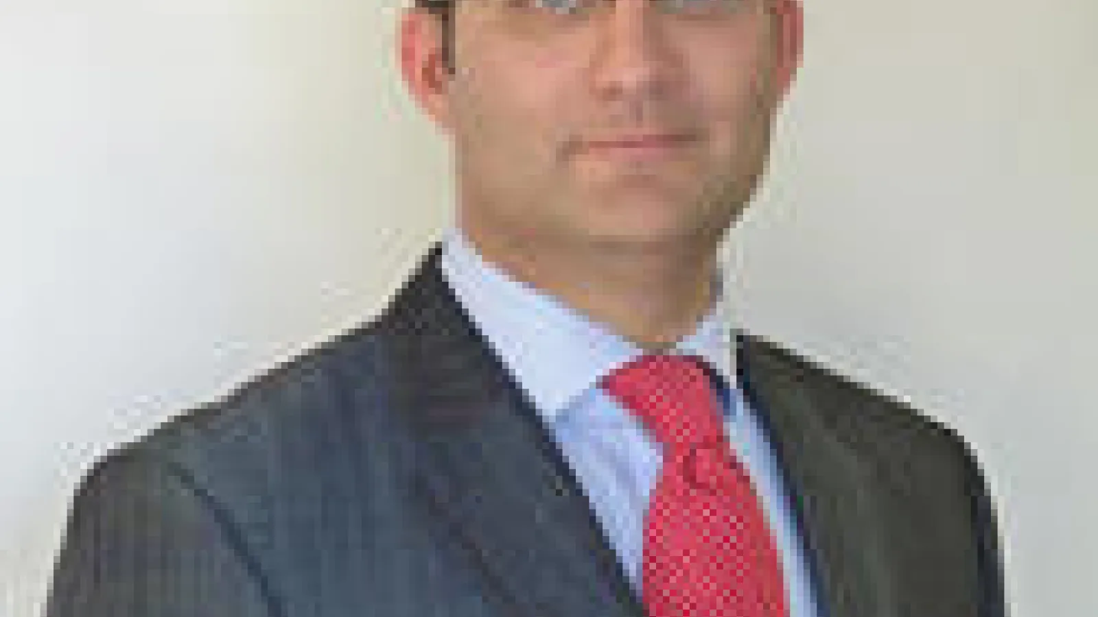 A brown haired blue eyed man in glasses with a red tie and blue sport coat