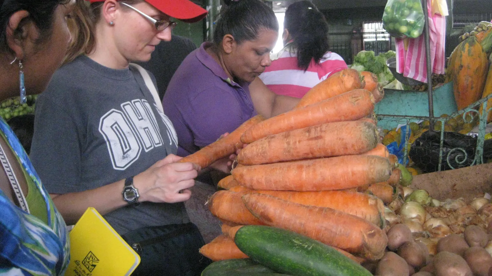 student in red ball cap inspecting vegetables at a market