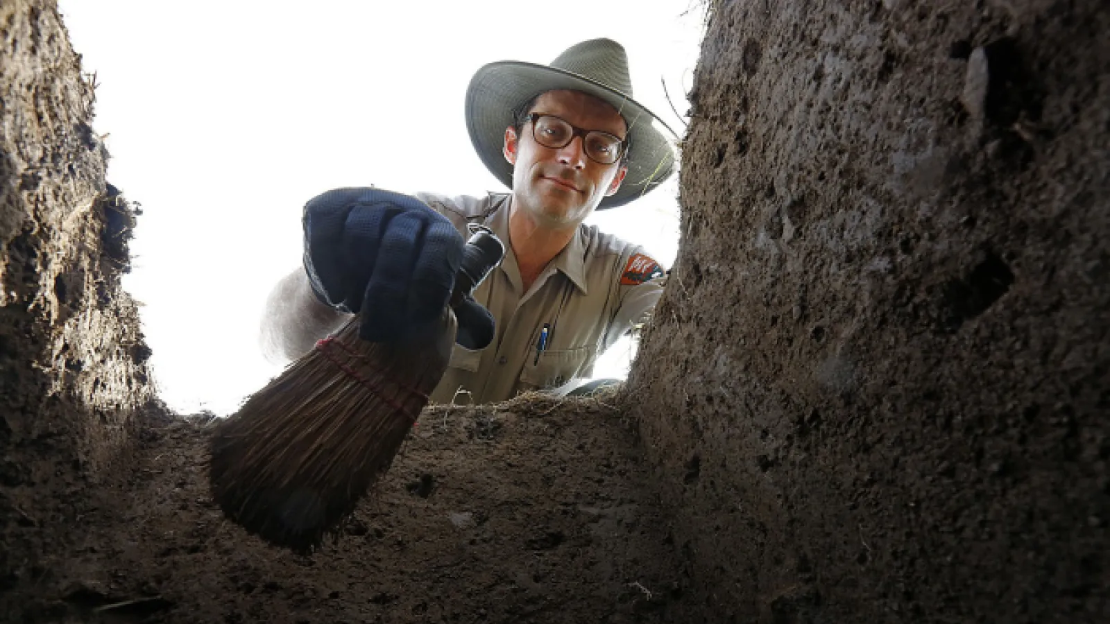 Man with hat looking into archaeological excavation pit at Hopewell Mound