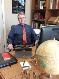 White man sitting behind a desk with a globe on it