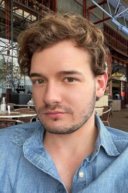 Steven Rhue headshot. He is a fair-skinned male with wavy but short hair, a beard and mustache and is wearing a denim dress shirt