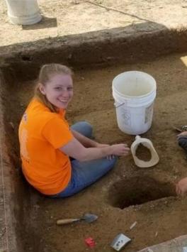 White woman sitting in a field site with a white bucket