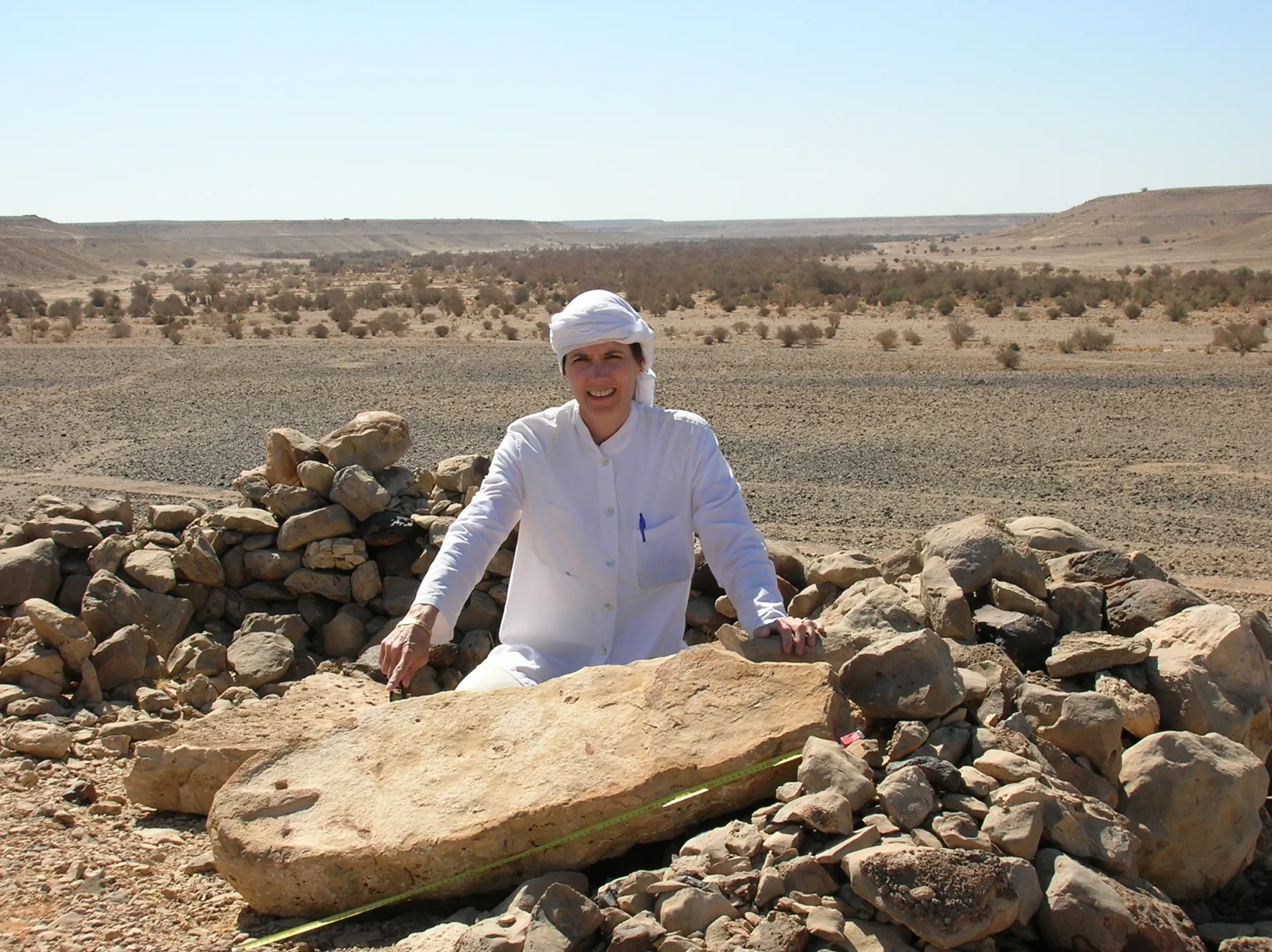 Man dressed in white pointing to an excavated carved stone