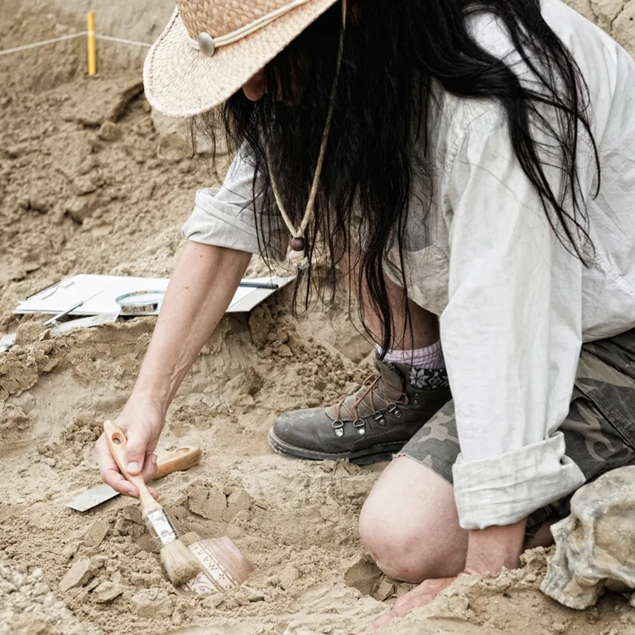Woman with long dark hair brushing dust off pottery in a field
