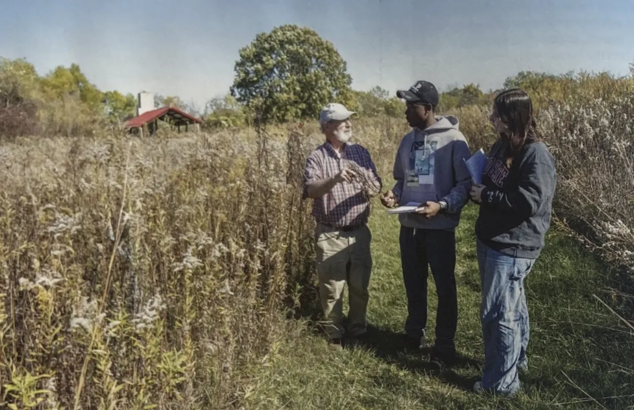 3 individuals standing in a farm field, talking with each other