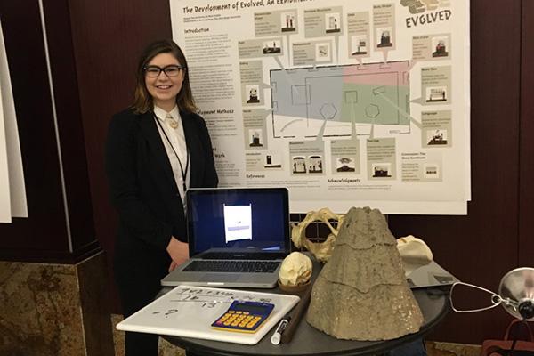 alumna Abbey Sarver-Verhey stands in front of poster displaying proposed museum exhibit