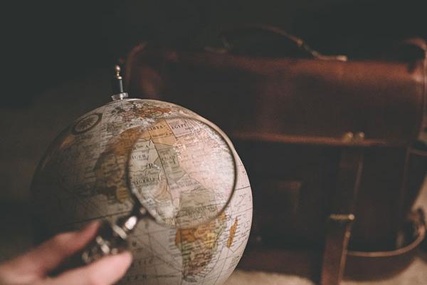 a hand holding a magnifying glass above a globe