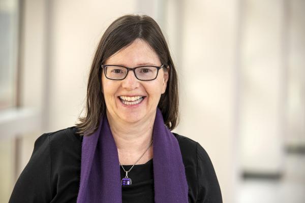 Headshot of Janet Childerhose. She is a white woman wearing glasses with shoulder length hair. She is wearing a black blouse and purple scarf
