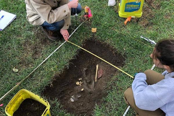 ANTHROP5686 This image shows two students over a small "grave" that they excavated for their class ANTHROP5686. They are planning the location of several pieces of evidence, including plaster casts of bones.