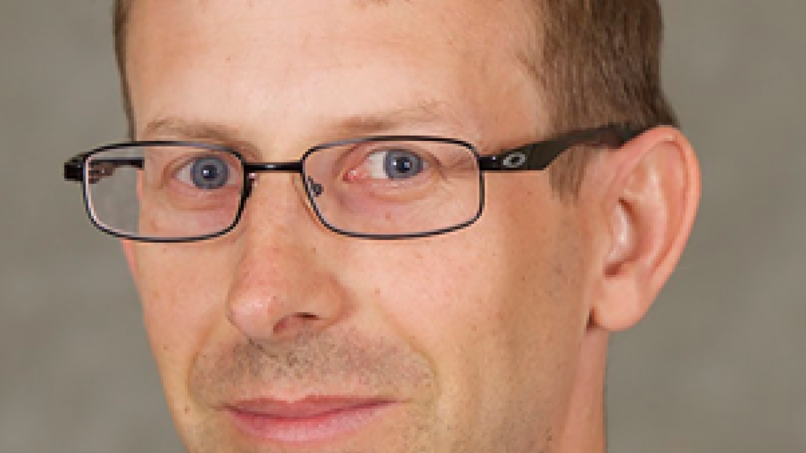 A man with very short dark hair wearing glasses