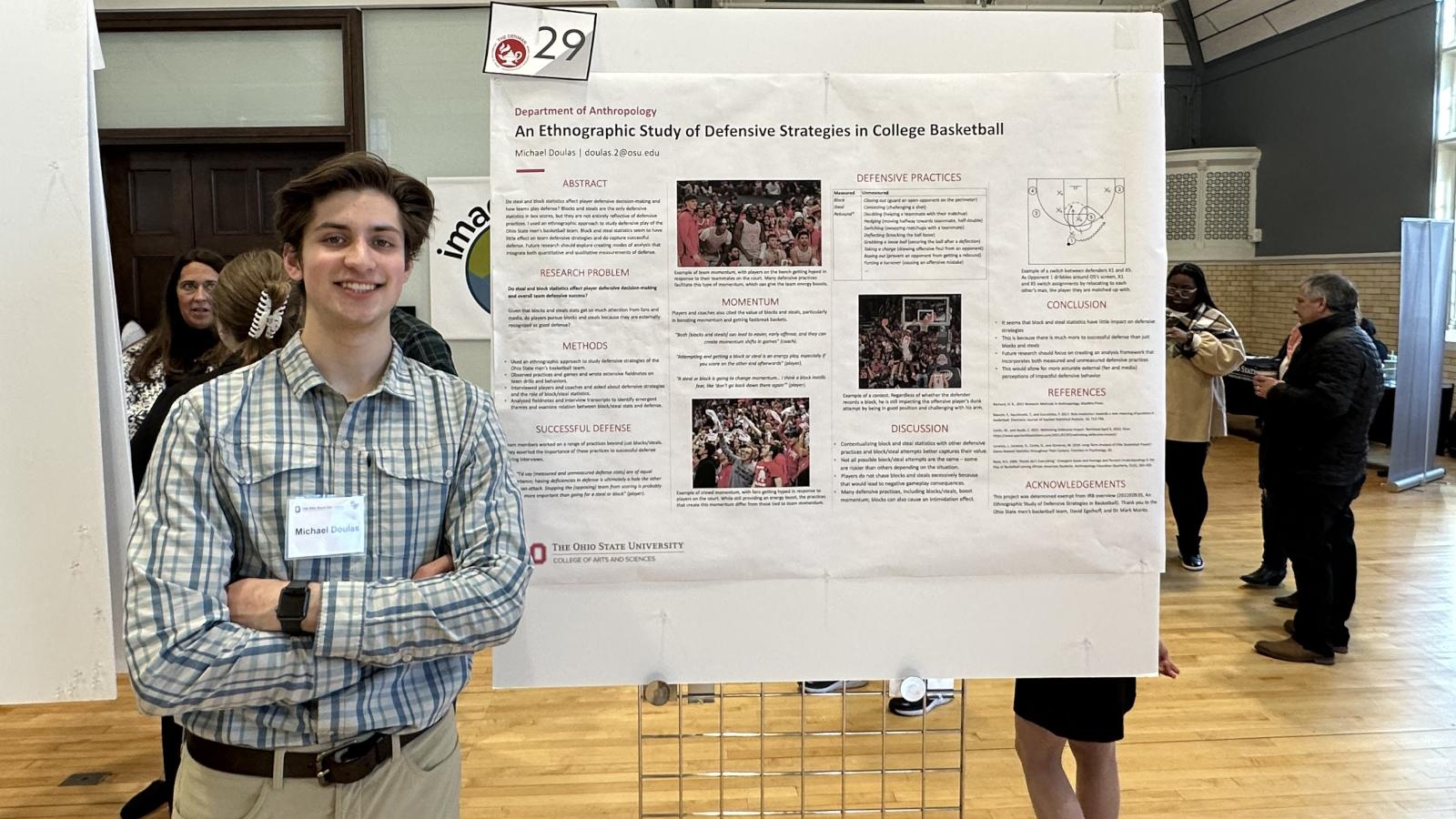 Dark haired man standing in front ot a poster presenting his research