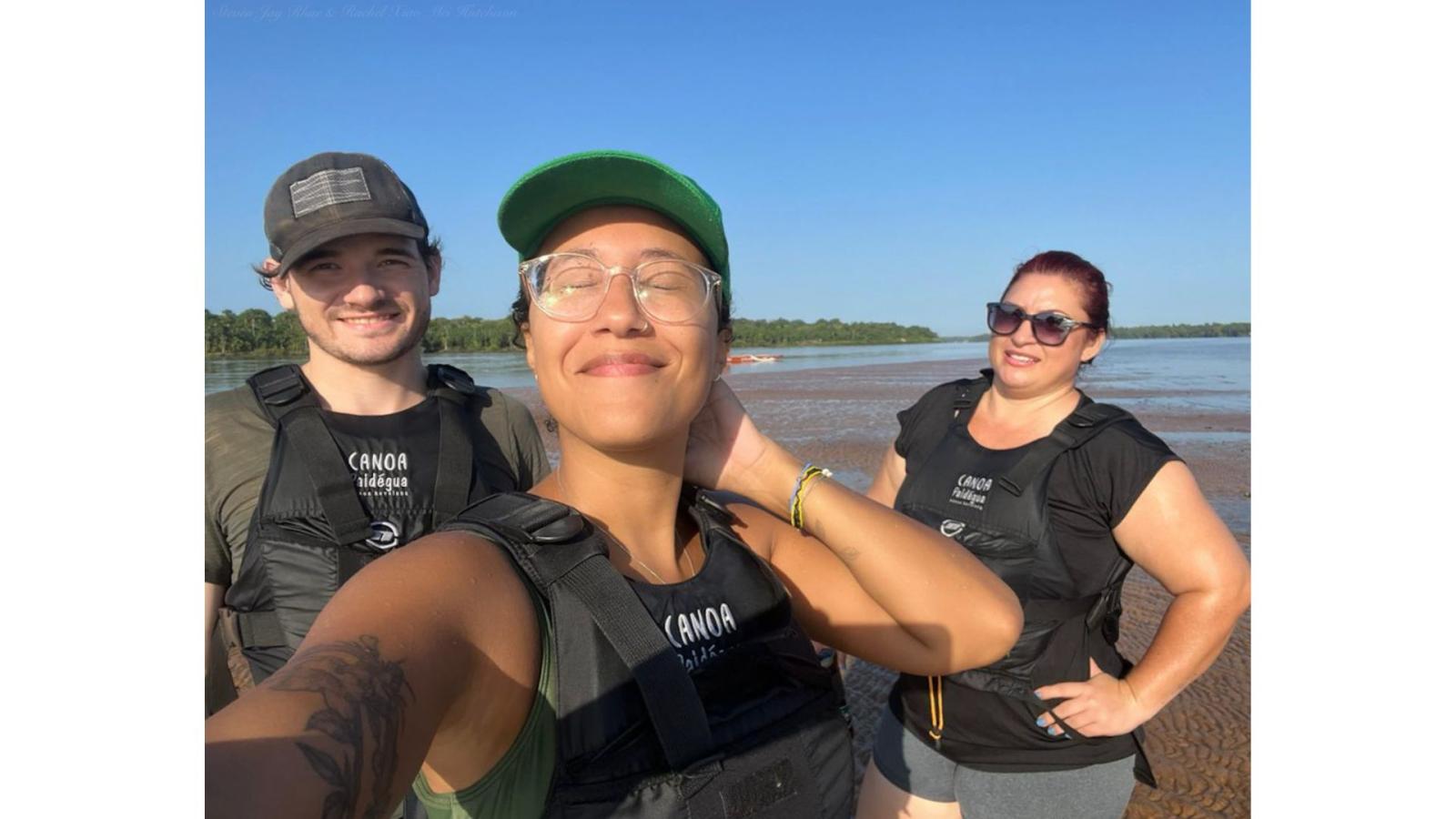 A young man and two young women standing on a sandbar