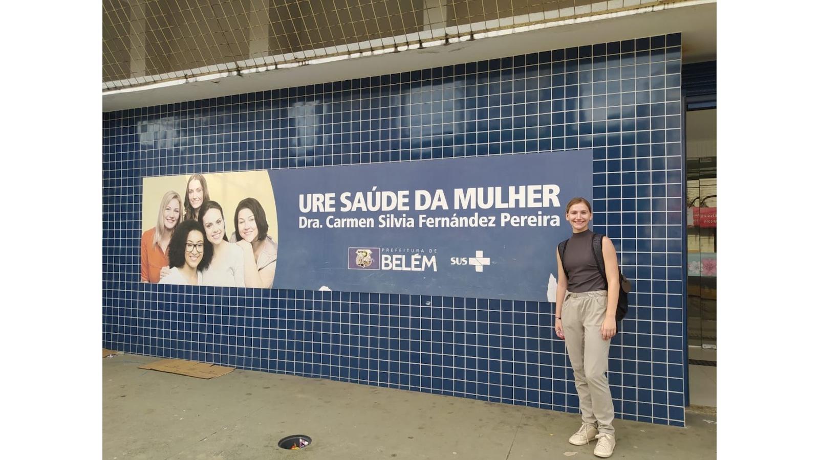 A young woman in a blue top and white pants standing in front of a tile wall