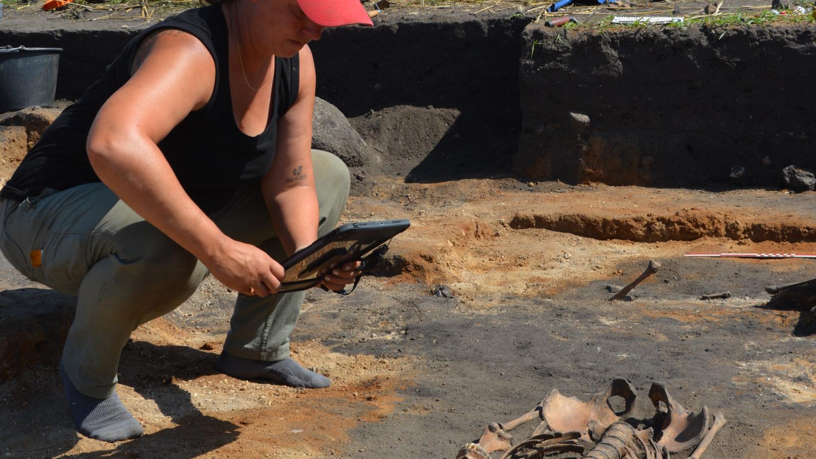 Woman in red hat taking a photo of an excavated skeleton