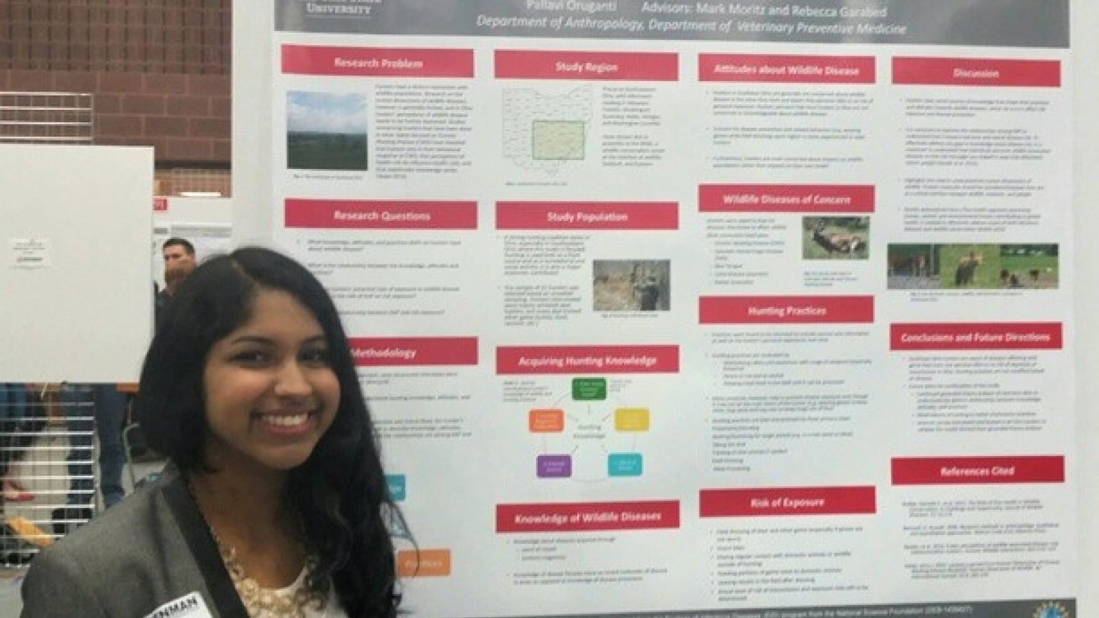 Smiling undergraduate student standing with her poster at the Denman Undergraduate Research Forum