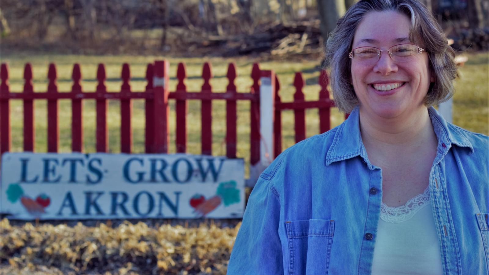 Smiling woman with glasses in front of a "let's grow Akron" sign