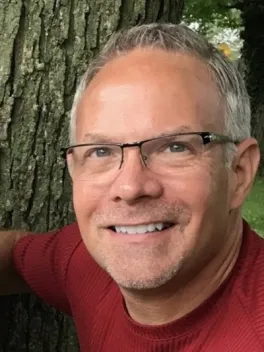 Smiling grey haired man in glasses and a red shirt